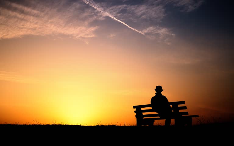 有一个男人坐在长椅上看夕阳西下