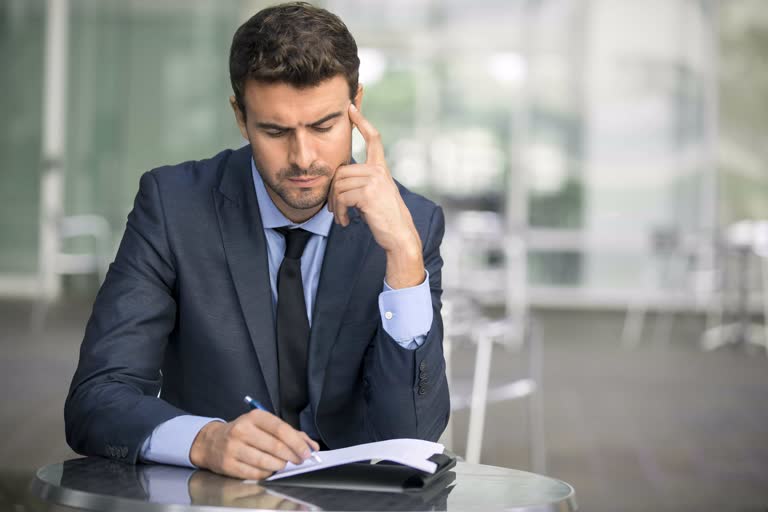 有一个西装革履、打领带的男人坐在一张桌子旁,手里拿着一本书