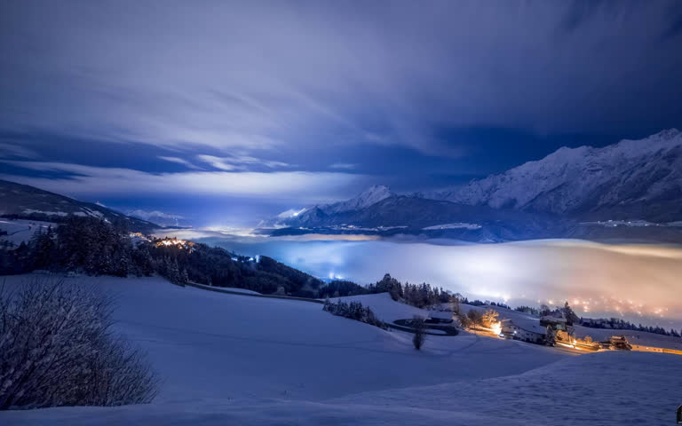 夜间白雪皑皑的山峦,远处有一座小镇