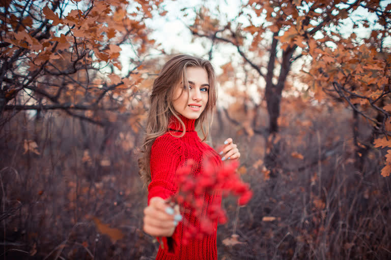 有一个穿着红色毛衣的女人,手里拿着一束红色的花