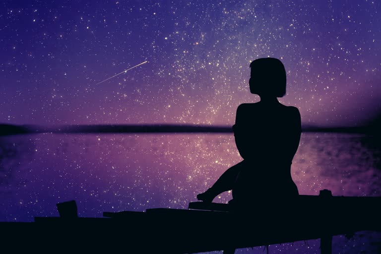 有一个女人坐在码头上看星星的剪影