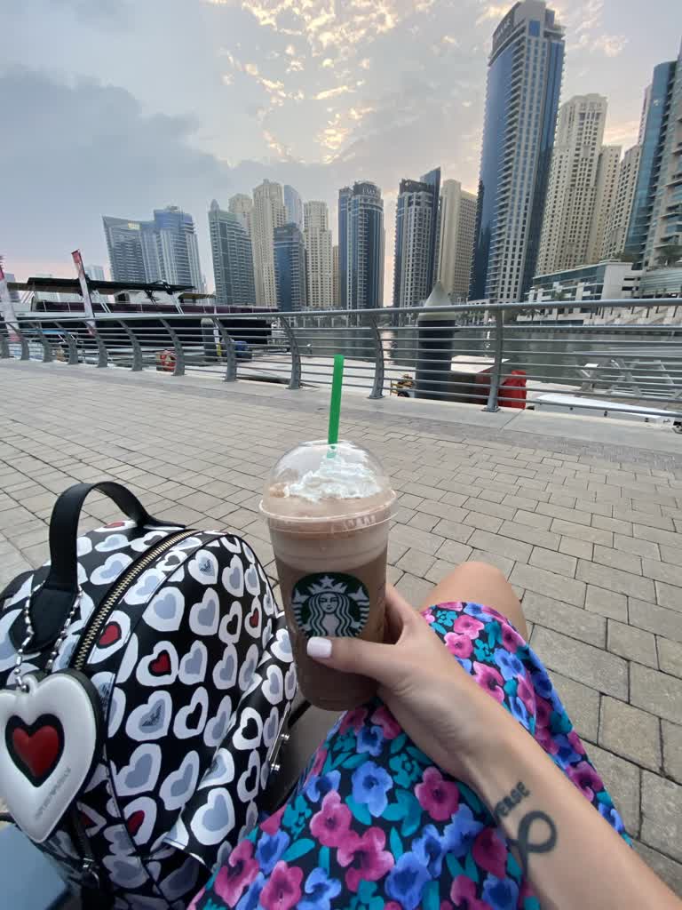 有一个女人坐在长凳上,手里拿着一杯咖啡