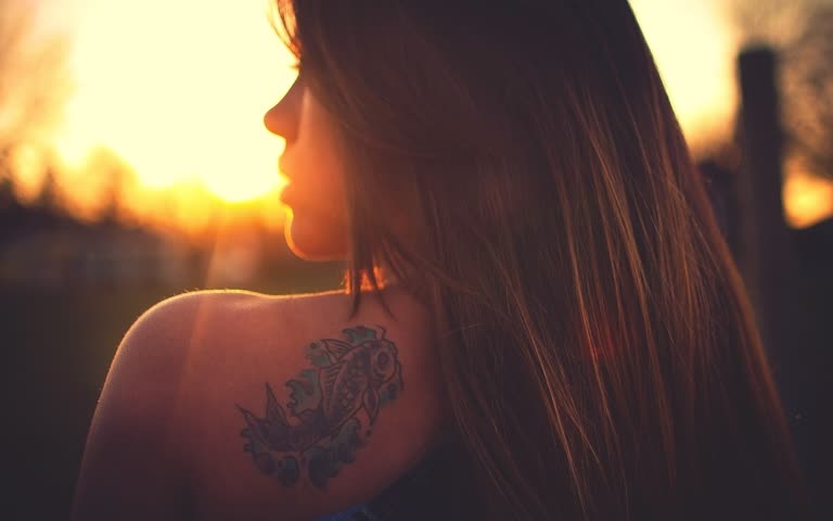有一个背上有纹身的女人看着夕阳